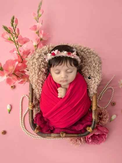 This little one looks so serene, wrapped in red and surrounded by delicate flowers. The overhead angle provides a lovely view of the entire setup.
