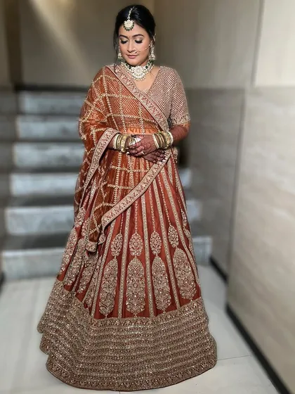 A full-length shot of the bride in her stunning rust-colored lehenga. The makeup is designed to complement the unique color palette, with warm tones and a radiant finish.