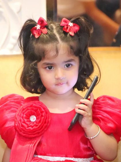 A cute portrait of a little girl in a bright red dress, holding a stylus like a phone.