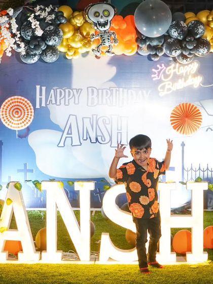The birthday boy takes center stage. Here's Ansh posing excitedly in front of his name in lights against a spooky and fun Halloween-themed backdrop.