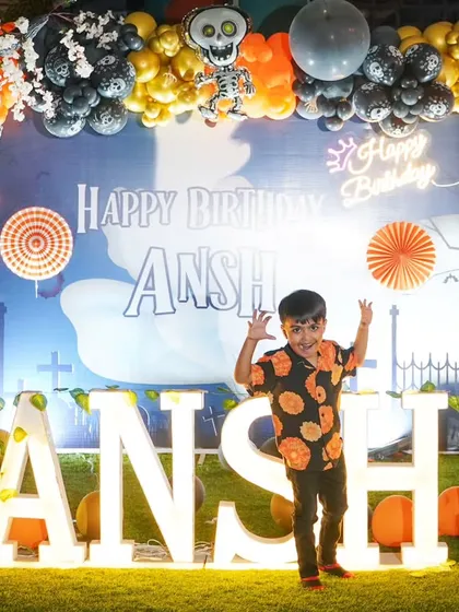 The birthday boy takes center stage. Here's Ansh posing excitedly in front of his name in lights against a spooky and fun Halloween-themed backdrop.