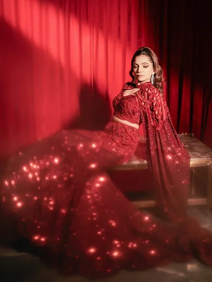 The ruby red lehenga catches the light, showcasing the sparkle of its full embellishment. A look designed for grace and glamour.