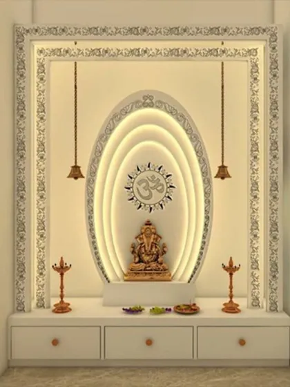 This contemporary mandir design features a central Ganesha idol set against a multi-layered, oval-shaped backlit panel. The clean lines, warm lighting, and minimalist frame with hanging bells create a modern yet devotional atmosphere.