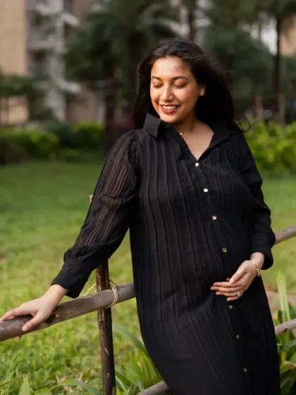 A casual and elegant portrait of the mom-to-be leaning against a railing, showcasing her beautiful baby bump in a stylish black dress.