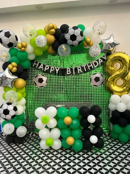 Another angle of a football theme party setup, this one on a rooftop. The green sequin backdrop mimics a football field, framed by a balloon arch with football and star-shaped foil balloons.