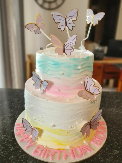 A two-tier cake with a soft watercolor buttercream effect and delicate butterflies, inspired by the birthday girl's dress.