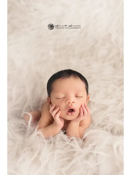 The classic "hands on cheeks" pose. This simple, unadorned shot on a soft, fluffy blanket highlights the baby's perfect features and peaceful expression.