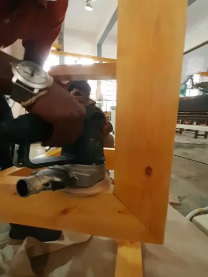 A student uses an orbital sander to smooth the surface of a wooden frame, an essential step in preparing a project for finishing.