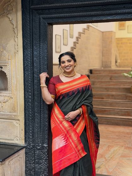 A striking look for a TV show promotion. The dark saree with a red border is complemented by a warm, subtle makeup palette and a simple gold necklace.