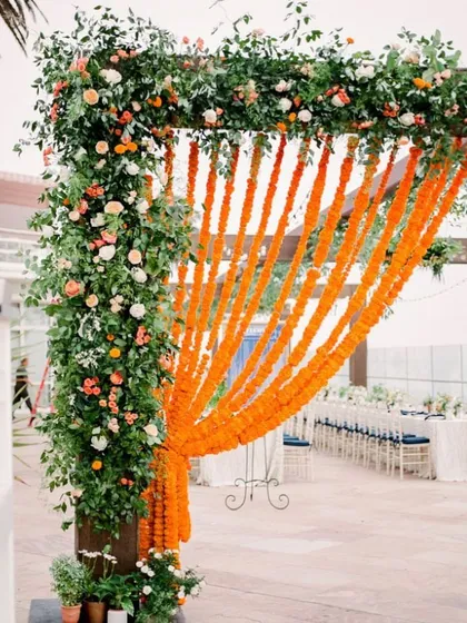 This is an entrance I created for an outdoor event, using a simple wooden frame. I decorated it with lush greenery and flowers, and added a curtain of bright orange marigold strings for a pop of traditional color.