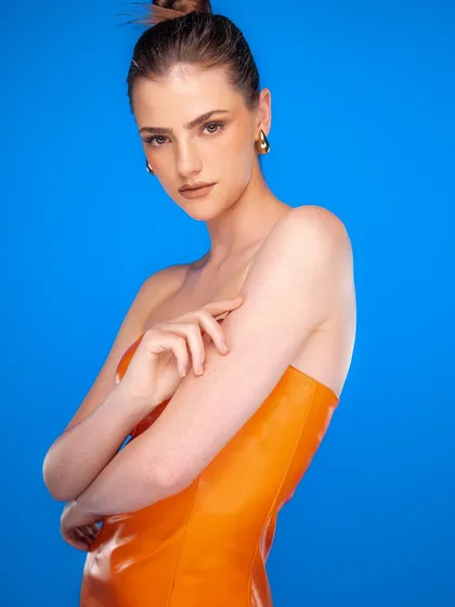 A vibrant and striking shot using a solid blue background to make the orange dress pop. The clean, high-key lighting creates a modern, graphic, and energetic feel.