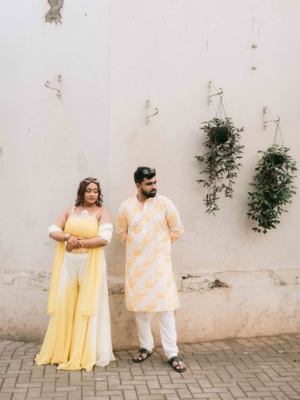 A stylish, full-length portrait of Nikita and Harsh. Their coordinated outfits and the clean, architectural background give this image a modern and minimalist aesthetic.