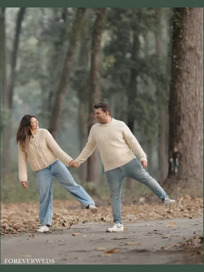 The same joyful moment from a different angle. This full-length shot shows off the beautiful autumn setting and the couple's coordinated casual style, adding context to their playful interaction.