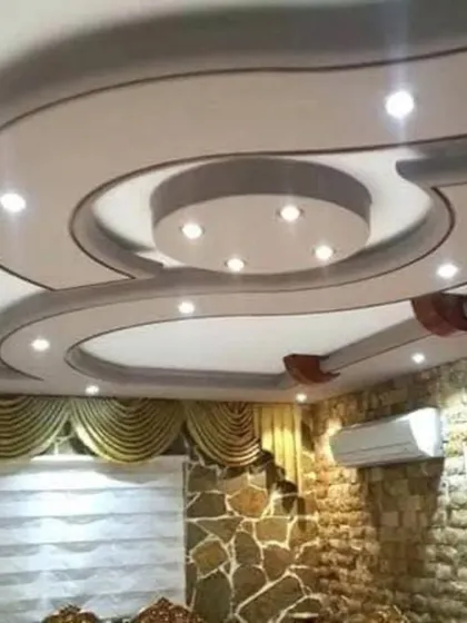 This grand, flowing design uses sweeping curves and multiple levels to create a dramatic effect. The integrated spotlights and the stone-cladded wall in the room complement the luxurious feel of the ceiling.