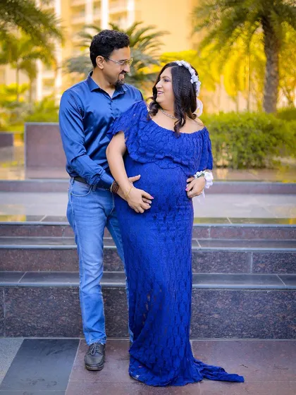 A full-length portrait of the couple during their outdoor maternity shoot. The vibrant blue dress stands out beautifully against the natural background.