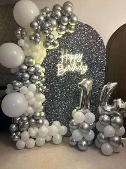 A glamorous 14th birthday with a silver sequin backdrop, a white and silver balloon arch, and silver foil number balloons.