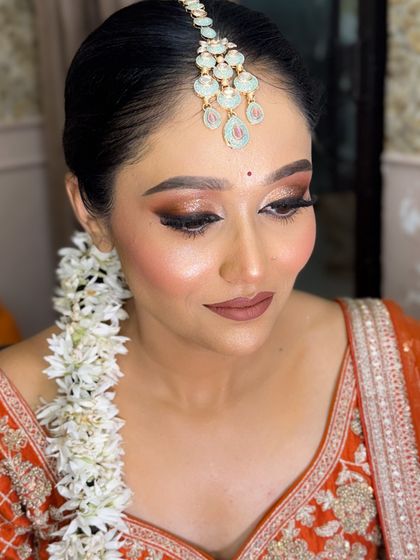 Another beautiful shot of the bride in the orange lehenga, highlighting her glowing skin and the intricate details of her maang tikka.