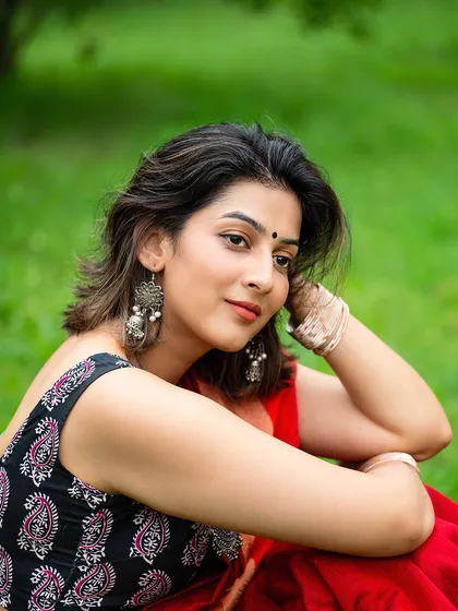 A relaxed, seated portrait of the model in a saree, showcasing her traditional jewelry and a gentle expression. This image has a soft, graceful quality.