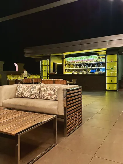 Another perspective of the lounge area at the rooftop cafe, showing the custom-designed slatted wood sofa and its proximity to the illuminated bar. This demonstrates our approach to creating cohesive outdoor commercial spaces.