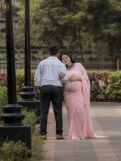 A quiet moment in a park, with the mom-to-be in a pink saree resting her head on her partner's shoulder.