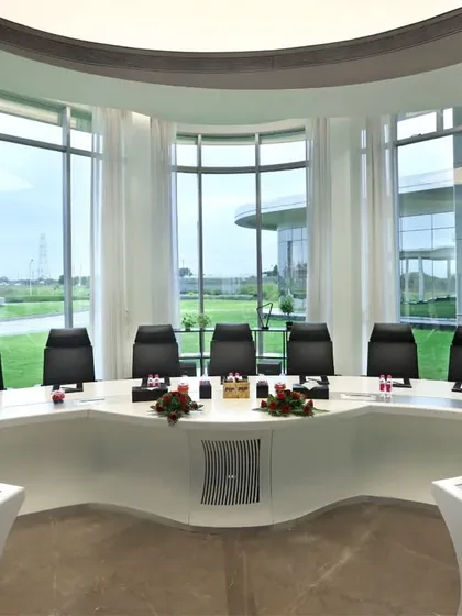 A futuristic, circular boardroom with a custom-designed conference table. The expansive windows flood the space with natural light and provide an unobstructed view, creating a powerful setting for high-level meetings.