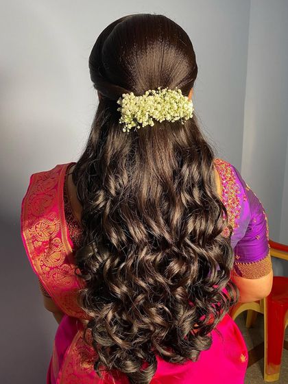A reception hairstyle with soft curls and a half-updo, adorned with a simple bar of fresh baby's breath.