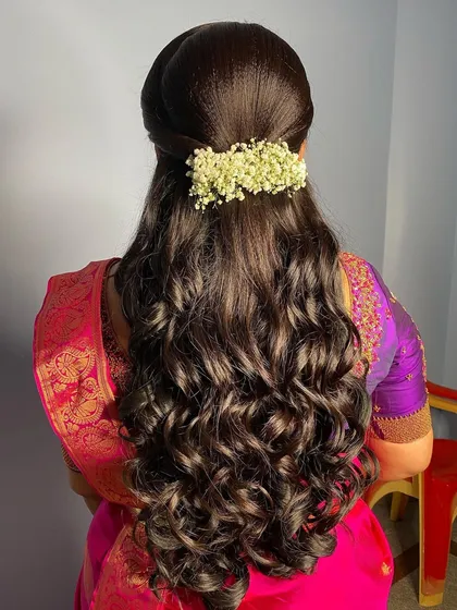 A beautiful half-updo with soft curls, adorned with a fresh jasmine gajra. This is a classic and elegant hairstyle that is perfect for a reception or engagement.