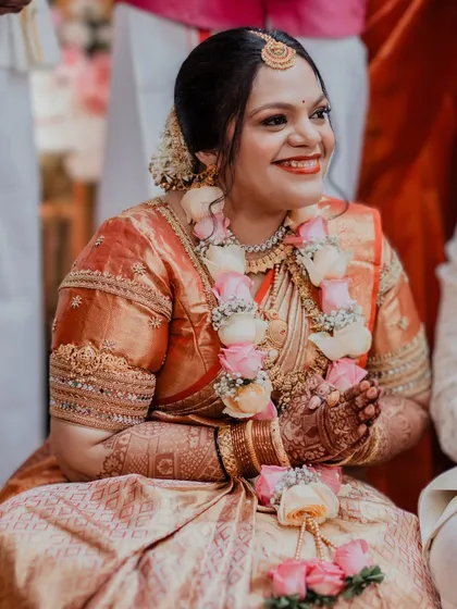 A candid, joyful moment from a wedding ceremony. The bride's makeup is radiant and warm, with a classic red-orange lip that perfectly suits the festive occasion.