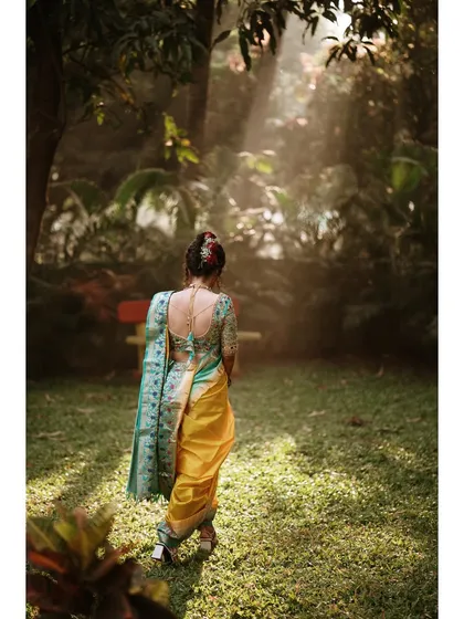 A beautiful back-shot of the bride walking into a sunlit garden. This portrait highlights the intricate design of her blouse and her graceful posture.