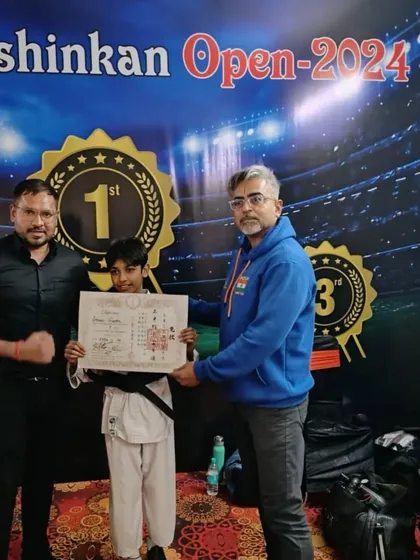 Ishaan holding his black belt certificate alongside his coaches. This represents the culmination of his training and the beginning of a new chapter in his martial arts path.