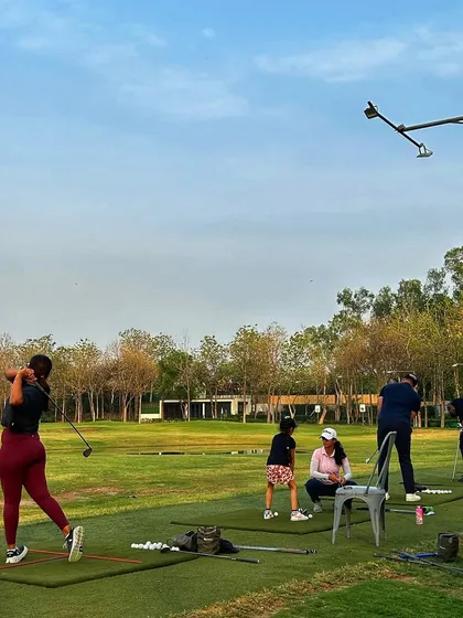 A female golfer unleashes a powerful swing on the grass tee, with her friends watching on.