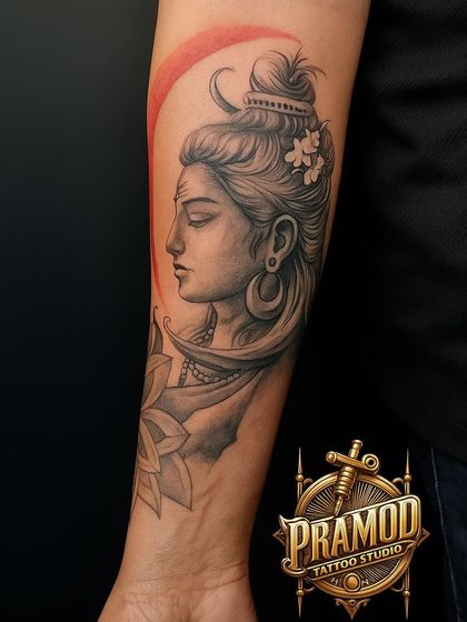 This tattoo combines a serene portrait of Shiva with a lotus flower, symbolizing purity and enlightenment. The red background adds a touch of modern artistry, making the black and grey work stand out beautifully.