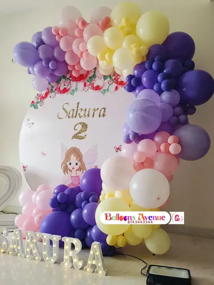 A Sakura-themed second birthday party with a beautiful floral backdrop. The balloon arch uses shades of purple, pink, and yellow to match the cherry blossom concept.