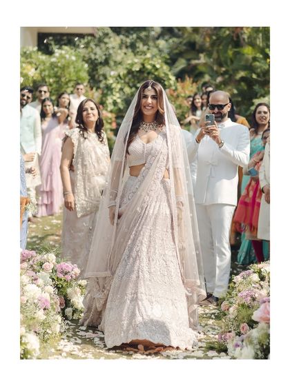The bride's grand entrance down a petal-strewn aisle in her home garden. Her radiant smile and the beautiful setting make this a breathtaking ceremony moment.