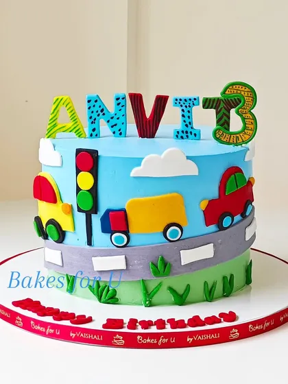 A fun and colorful vehicle-themed cake for a 3rd birthday. This design features a fondant road with cars, a truck, and a traffic light, perfect for any little one who loves things that go.
