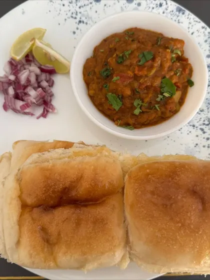 A plate of our delicious, home-style Pav Bhaji. We make the bhaji with a rich blend of fresh vegetables and our special spice mix, served with soft, buttered pav buns, chopped onions, and a slice of lemon.