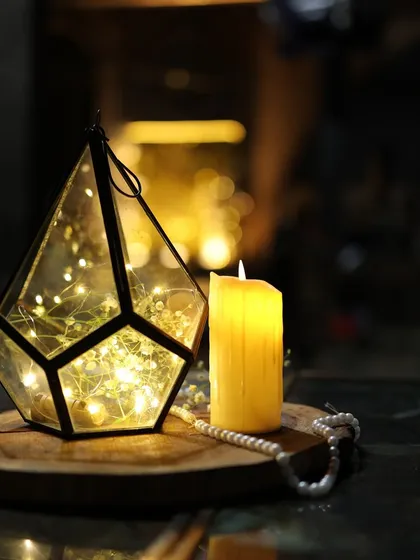 A simple yet beautiful centerpiece detail. A geometric lantern filled with fairy lights and baby's breath, placed next to a candle, adds a touch of magic and warmth to the table.