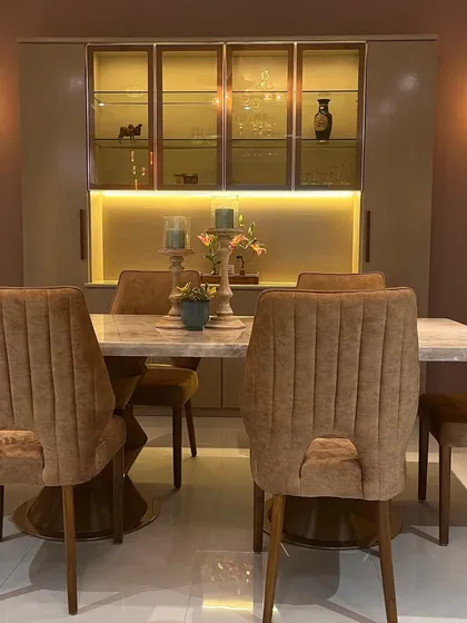 This elegant dining area features a marble-top table and plush upholstered chairs. The back-lit crockery unit with glass and profile shutters adds a touch of sophistication and provides beautiful display storage.