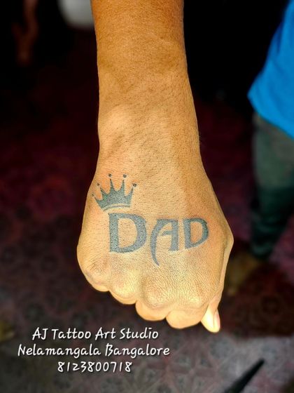 A bold "DAD" tattoo with a crown on the back of the hand.
