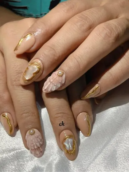 A close-up of my seashell-inspired nails. The design features a nude base, gold chrome accents, and textured 3D shells with pearl details.