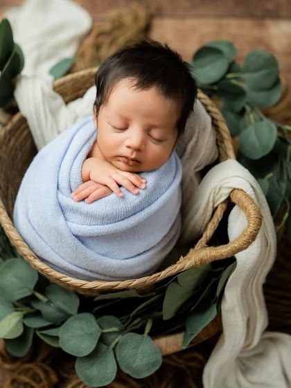 This classic wrapped pose in a basket is a staple of newborn photography. The soft blue tones and natural elements create a timeless and serene image.