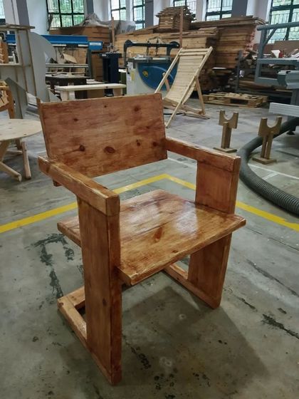 A finished solid wood chair with a bold, minimalist design. The piece has been stained and polished, highlighting the natural grain of the wood.
