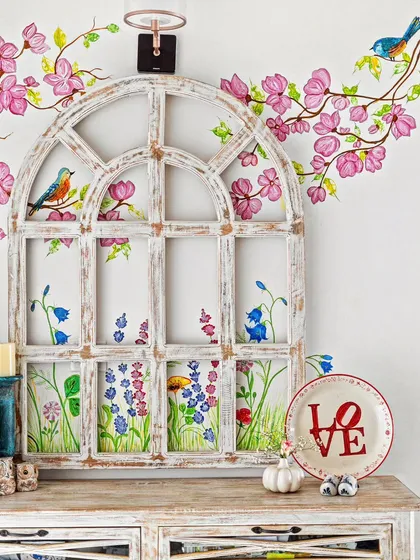 A charming console setup with a distressed white window frame and hand-painted floral art on the wall. This detail shot captures the whimsical and artistic Santorini vibe of the villa.