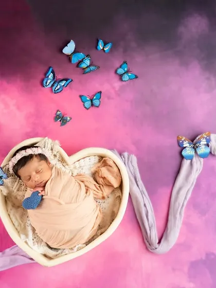 A creative 'LOVE' themed setup where the baby sleeps in a heart-shaped basket, with the letters formed from purple fabric and accented with butterflies.