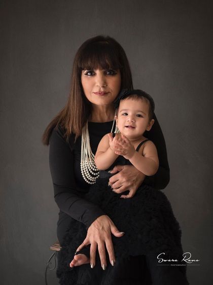 A classic portrait of a glamorous grandmother holding her adorable granddaughter. Both are looking at the camera, creating a cherished memory for the family.