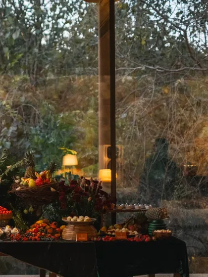 A grazing table set against the large glass windows of our Pavilion, with the forest visible outside. The table is laden with fruits, desserts, and canapés, creating a feast for the senses.