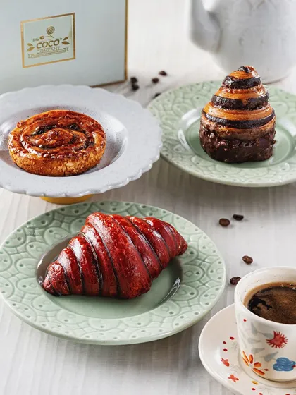 A trio of gourmet pastries, including a vibrant red croissant and a chocolate swirl. This image highlights the bakery's creative and colorful offerings, paired with coffee for a perfect breakfast scene.
