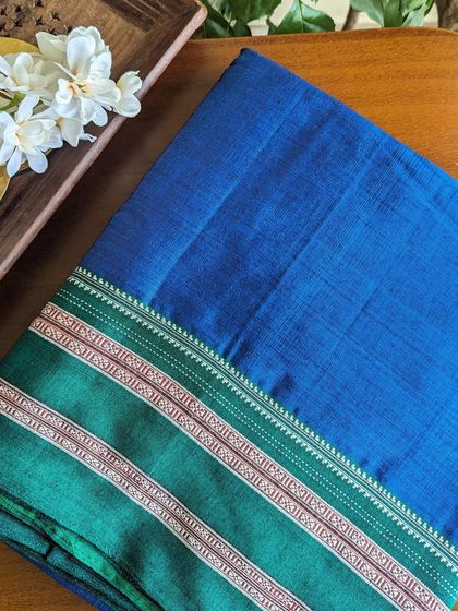 This Ilkal saree features a stunning royal blue body with a contrasting green border, woven with intricate traditional designs.