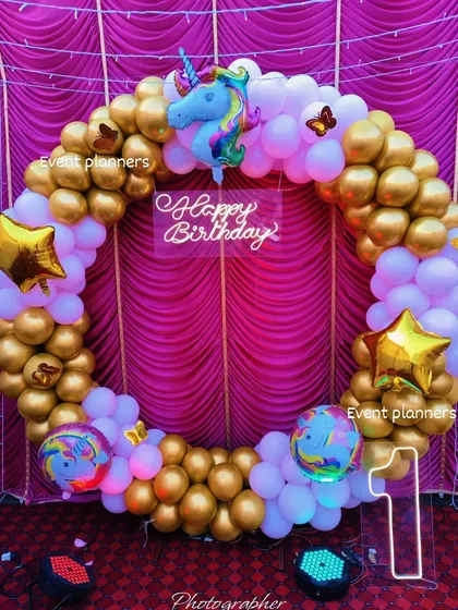 A glamorous first birthday setup with a gold and white balloon circle, unicorn accent, and neon sign.