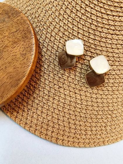 A styled shot of the classy minimal drop earrings against a woven hat, giving a chic, summery vibe.